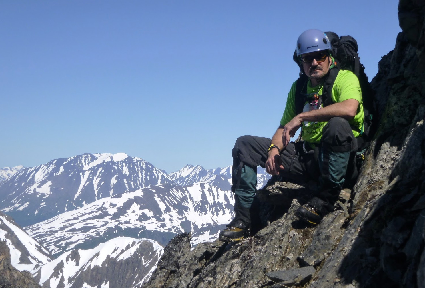 Dano Michaud sits on rocky crag of Mt Eva with snow covered mountains in background