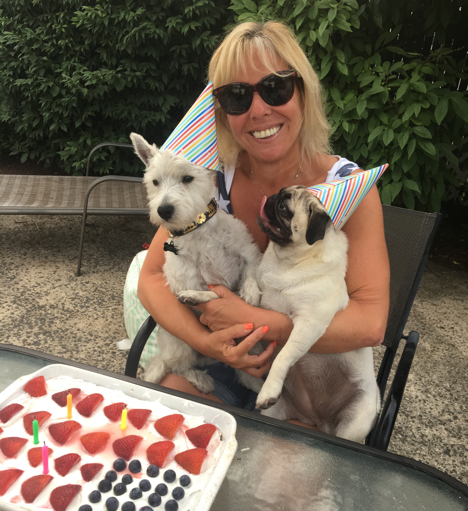 Woman holding two dogs wearing birthday hats sitting in front of table with birthday cake