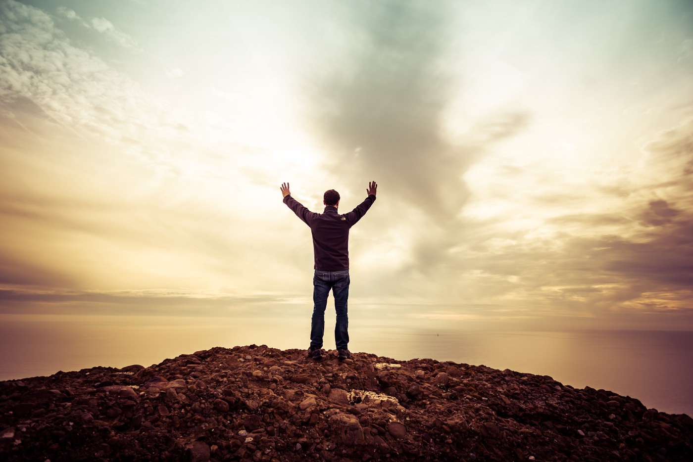 Man facing away to clouds with hands raised